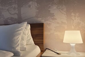 Ein ordentlich bezogenes Bett mit weißer Bettwäsche und einem Holz-Kopfteil, ein Nachttisch mit einer Lampe sowie eine Wand mit einem Baum-Muster.