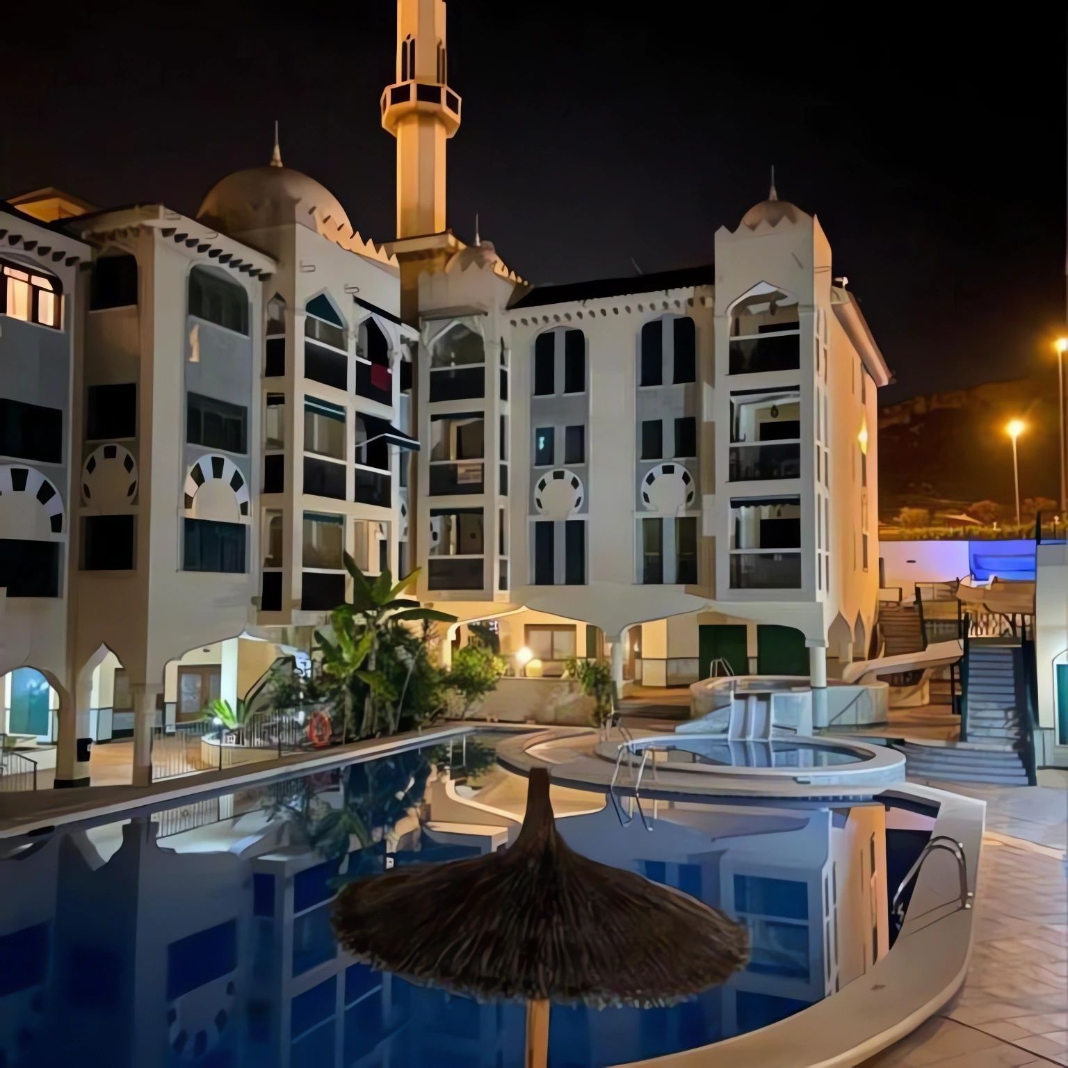 Un hotel con piscina, sombrilla de paja y un minarete.