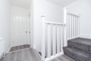 A hallway with a white door, a white railing, and a carpeted staircase. - 4 Bed House Harrow Near Wembley (Harrow)