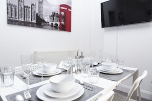 A dining table set with white plates, bowls, glasses, and cutlery, with a red telephone booth and a black TV screen in the background. - 4 Bed House Harrow Near Wembley (Harrow)