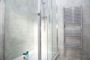 A modern bathroom with a glass shower enclosure, a chrome towel rack, and a tiled floor. - 4 Bed House Harrow Near Wembley (Harrow)