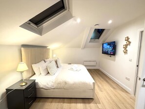 Ein Schlafzimmer mit Bett, Nachttisch, Lampe, Fernseher und einem Oberlicht.