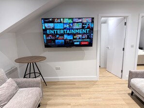 Uma sala de estar moderna com uma televisão de tela plana na parede, uma mesa de madeira redonda e dois sofás cinzentos.