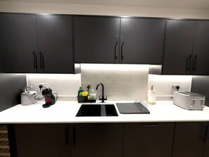 A modern kitchen with dark cabinets, a white countertop, a black faucet, a toaster, and a kettle. - 3 Bed Penthouse Near Airport & Trafford Centre (Wythenshawe)