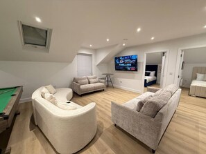 Ein großzügiger Wohnbereich mit Billardtisch, zwei Sofas, einem Fernseher und einer Billardausstattung.