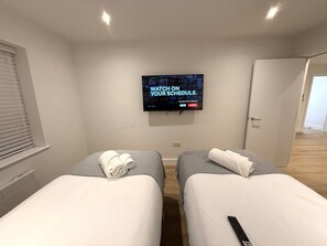 A hotel room with two beds, a television mounted on the wall, and a door to the right. - Twin+Sofa Bed in Sale Nr Airport & Trafford Centre (Wythenshawe)