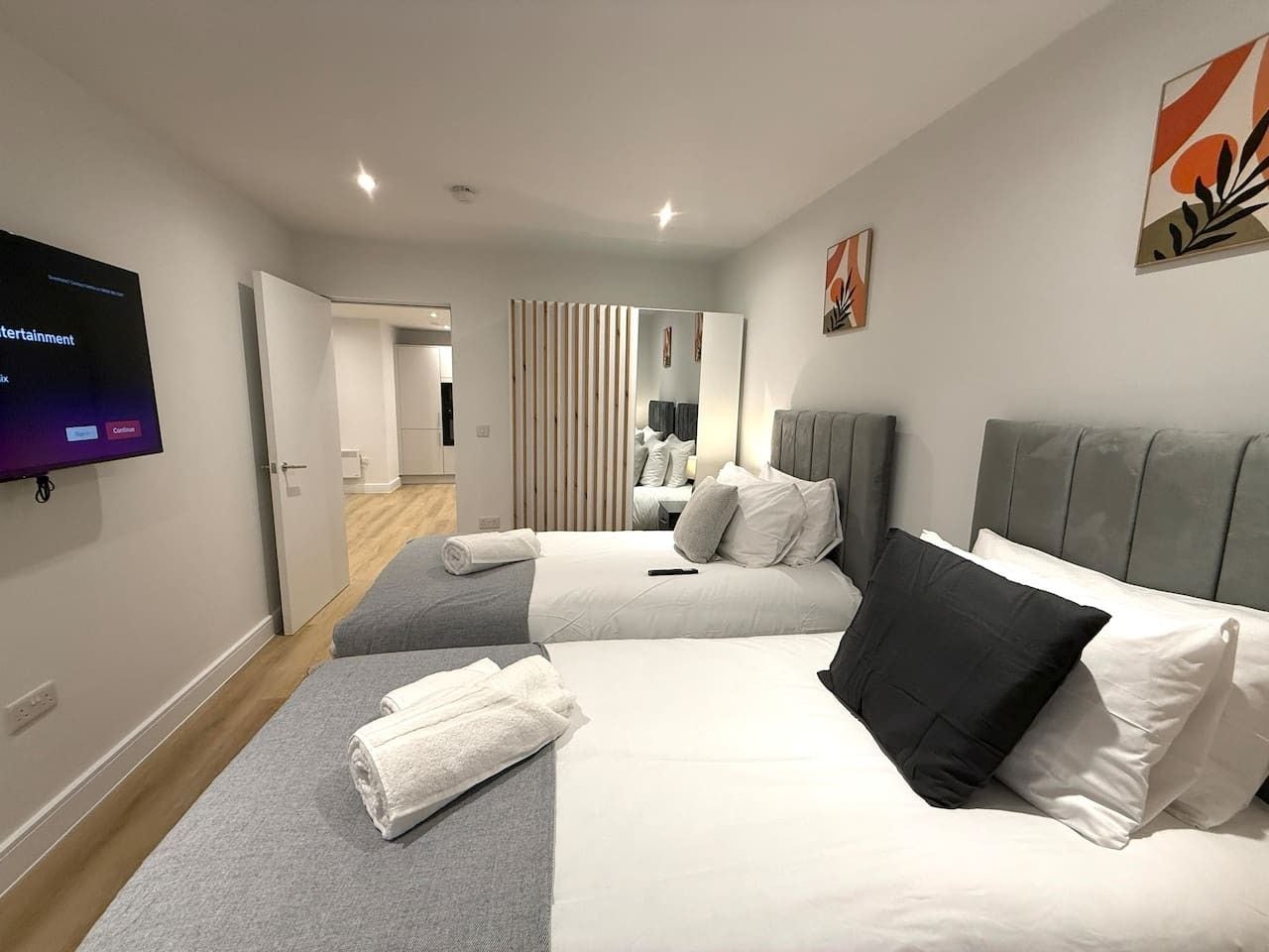A hotel room with two beds, a television, and a view of the hallway.