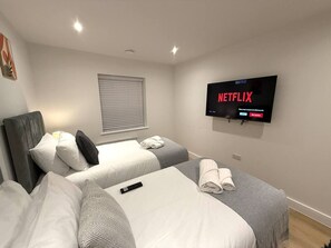Habitació d'hotel amb dos llits, una televisió penjada a la paret i una finestra amb persianes.