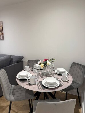 A dining area with a round table set for four, surrounded by grey upholstered chairs. - Twin+Sofa Bed in Sale Nr Airport & Trafford Centre (Wythenshawe)