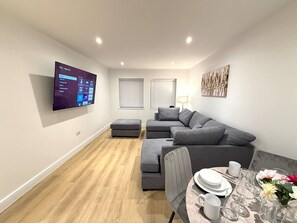 A modern living room with a sectional sofa, a dining table set for two, and a flat-screen TV mounted on the wall. - Twin+Sofa Bed in Sale Nr Airport & Trafford Centre (Wythenshawe)