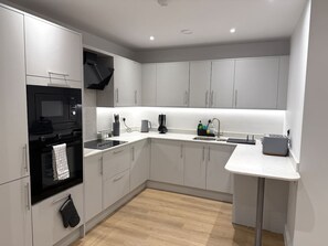 A modern kitchen with white cabinetry, a black oven, and a white countertop. - Twin+Sofa Bed in Sale Nr Airport & Trafford Centre (Wythenshawe)