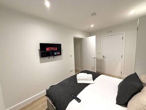 A hotel room with a bed, a TV mounted on the wall, and a door leading to another room. - 2 Bed+Sofa in Sale Near Airport & Trafford Centre (Wythenshawe)