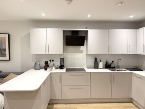 A modern kitchen with white cabinetry, a central island, and a built-in range hood. - 2 Bed+Sofa in Sale Near Airport & Trafford Centre (Wythenshawe)