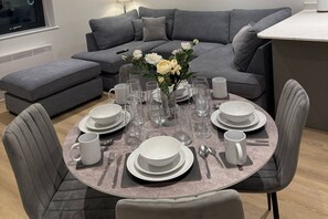 Een eetgedeelte met een ronde tafel gedekt voor zes personen, omringd door grijze fauteuils.