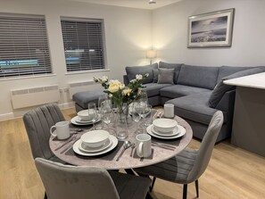 Un espace repas moderne avec une table ronde pour quatre personnes, un canapé gris et une lampe.