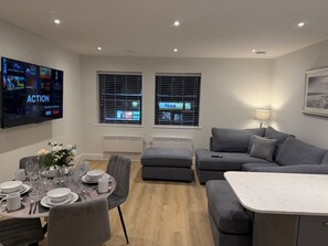 A modern living room with a dining area, grey sofas, a flat-screen TV, and a window with a view. - 1 Bed+Sofa in Sale Near Airport & Trafford Centre (Wythenshawe)
