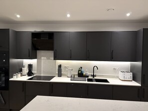 A modern kitchen with dark cabinets, a white countertop, and under-cabinet lighting. - 2 Bed+Sofa in Sale Near Airport & Trafford Centre (Wythenshawe)