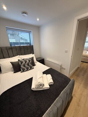 A neatly made bed with a dark headboard, white linens, and a folded towel on the bed. - 2 Bed+Sofa in Sale Near Airport & Trafford Centre (Wythenshawe)