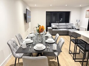 A modern dining area with a rectangular table set for four, surrounded by grey upholstered chairs. - 2 Bed+Sofa in Sale Near Airport & Trafford Centre (Wythenshawe)