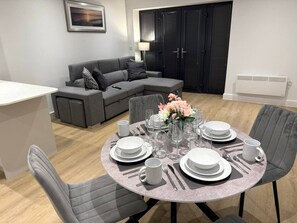 A dining area with a round table set for six, surrounded by grey upholstered chairs. - Twin+Sofa Bed in Sale Nr Airport & Trafford Centre (Wythenshawe)