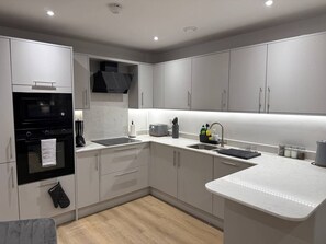 A modern kitchen with white cabinets, a black oven, a sink, and a countertop. - Twin+Sofa Bed in Sale Nr Airport & Trafford Centre (Wythenshawe)