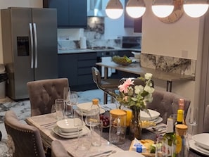 Un coin repas avec une table dressée pour quatre personnes, un réfrigérateur et une cuisine en arrière-plan.