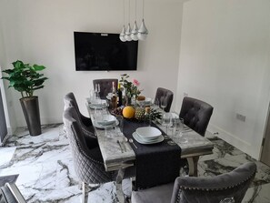 A dining room with a marble table, four chairs, a television above, and a potted plant.
