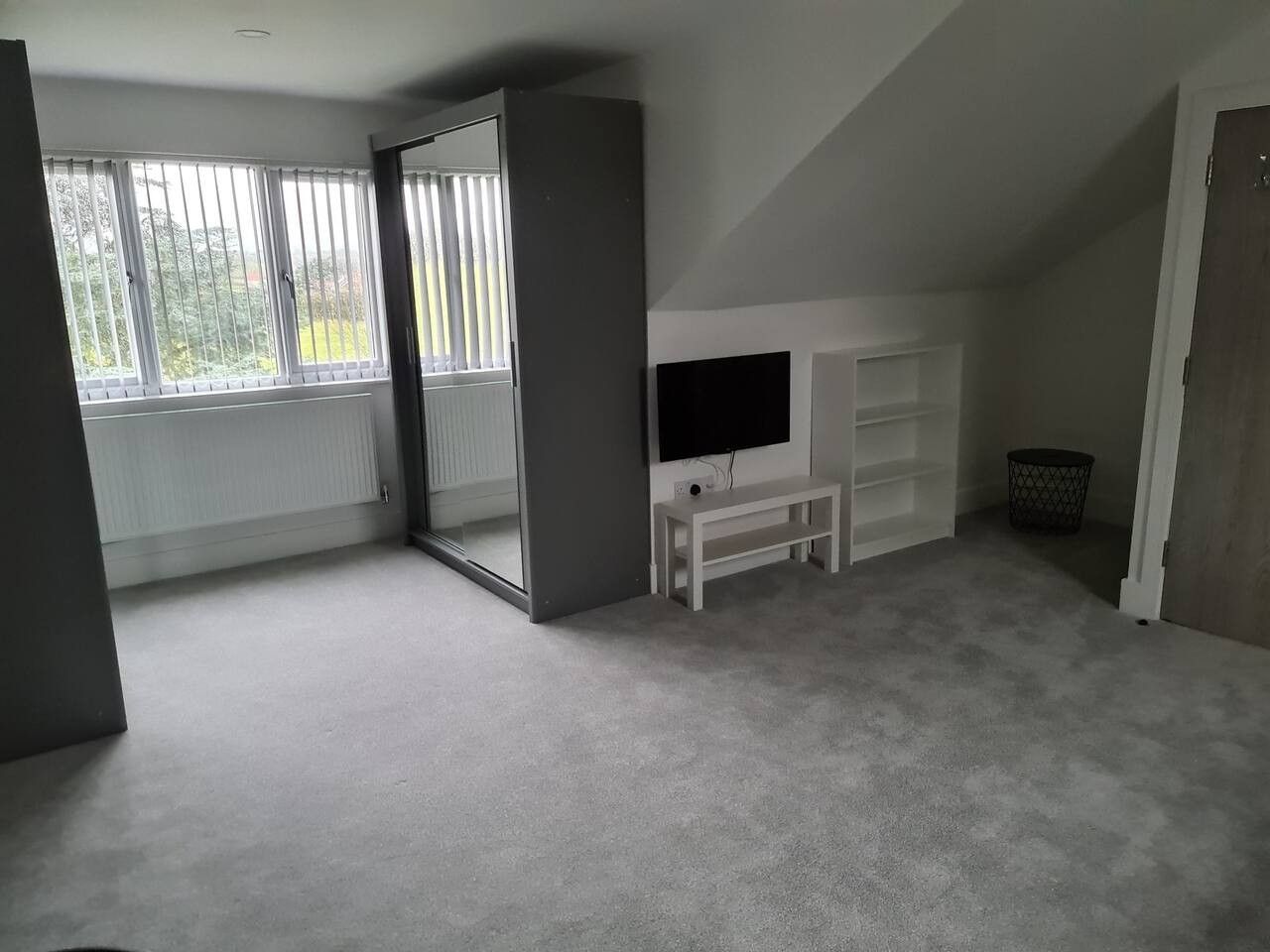 A room with a large window, a television, a white bench, and a storage unit.