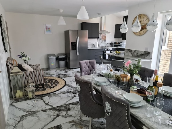 A modern kitchen with a marble floor, dining area with chairs, and a refrigerator.
