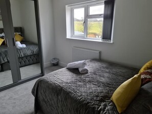 A bedroom with a bed, a window, a radiator, and a mirror.