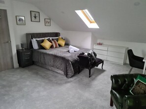 A bedroom with a bed, a nightstand, a chair, a desk, and a skylight.