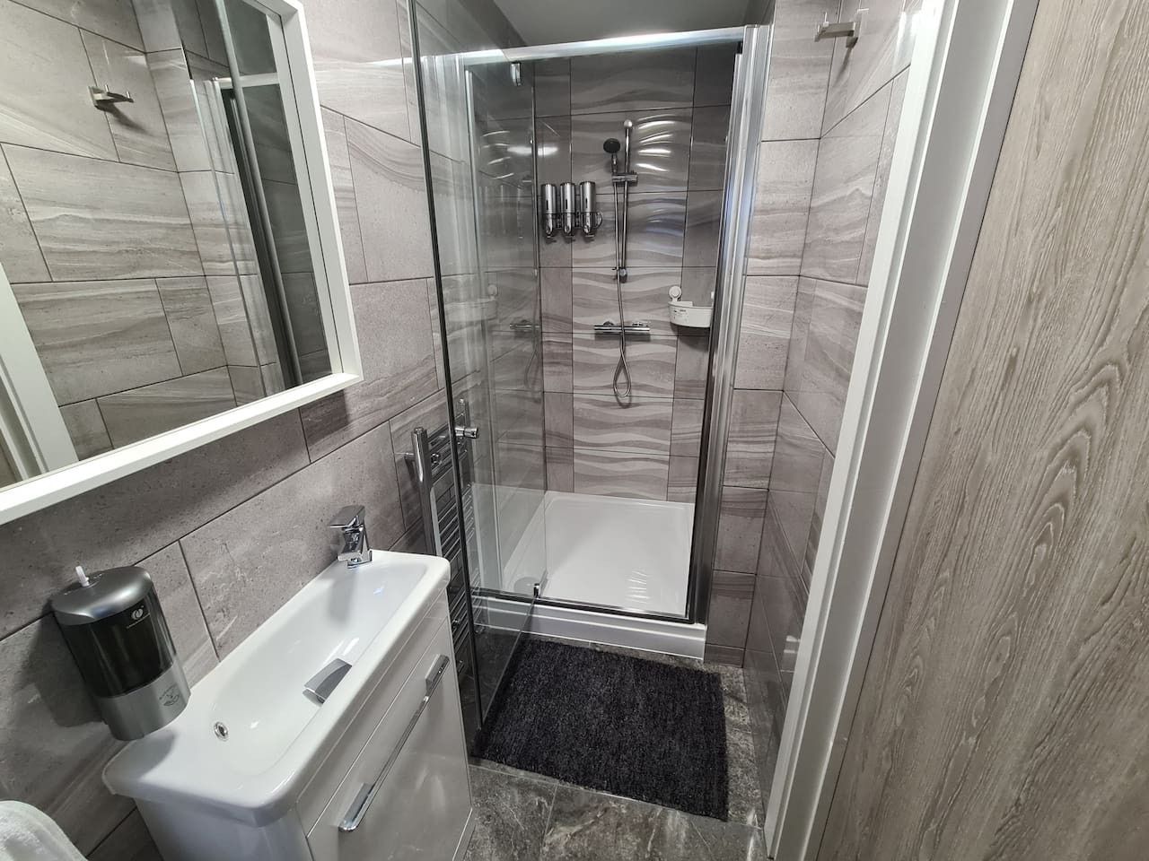 A modern bathroom with a glass-enclosed shower, a white bathtub, and a handheld showerhead.