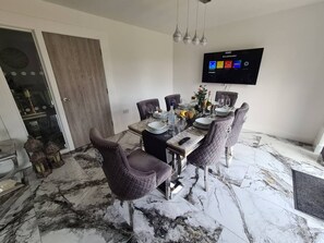 A dining area with a marble floor, a television mounted on the wall, and a door leading to another room. - SAV 5-Bed Executive Detached House, Leicester (Scraptoft)