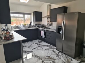 A modern kitchen with dark cabinetry, a stainless steel refrigerator, and a marble floor. - SAV 5-Bed Executive Detached House, Leicester (Scraptoft)