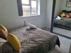 A bedroom with a bed, a window, a radiator, and a view through a glass door. - SAV 5-Bed Executive Detached House, Leicester (Scraptoft)