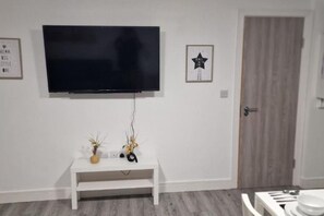 A room with a mounted television, a white console table with decorative items, and a door. - Sav Apartment Nottingham Road 1 bed Grd flr Flat (Leicestershire)