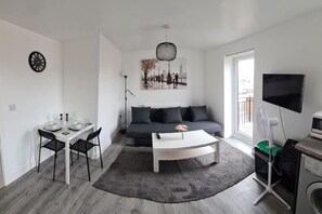 Ein modernes Wohnzimmer mit Essbereich, einem grauen Sofa, einem weißen Couchtisch, einem Flachbildfernseher und einer Waschmaschine.