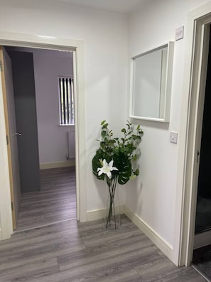 A hallway with a white door, a potted plant, and a window with vertical blinds. - Sav Stays Saffron Leicester - 2 Bed Apartment (Leicester)