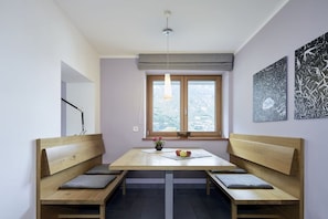 A room with a wooden dining table, benches, a hanging light fixture, a window with a view, and abstract wall art. - Schwarzlehen - Kirchbach (Naturns)