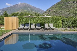 A swimming pool with lounge chairs and umbrellas, surrounded by greenery and mountains. - Schwarzlehen - Kirchbach (Naturns)