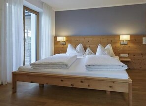 A bed with pillows and a blanket, a wooden headboard, two wall-mounted lamps, and a window with curtains. - Schwarzlehen - Kirchbach (Naturns)