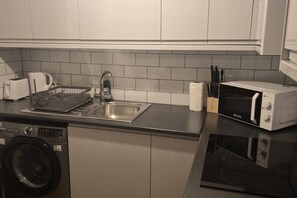 A compact kitchen with a stainless steel sink, a microwave, a toaster, and a dishwasher. - SAV 1 Bed Flat Near Watford Town (Hertfordshire)