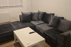 A modern living room with a sectional sofa, a small white table, and a remote control on the table. - SAV 1 Bed Flat Near Watford Town (Hertfordshire)