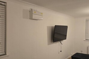 A room with a mounted air conditioner, a flat-screen TV, and a window with blinds. - SAV 1 Bed Flat Near Watford Town (Hertfordshire)
