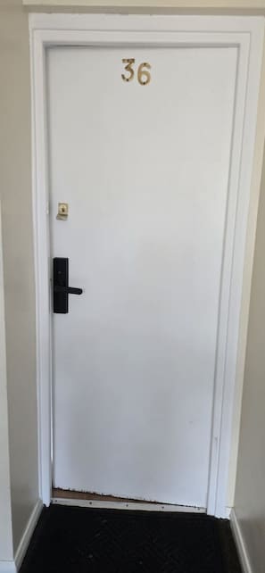 Eine weiße Tür mit der Nummer 36, einer schwarzen Türklinke und einem kleinen Messingschloss.