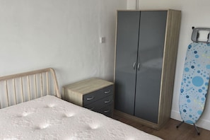 Ein Schlafzimmer mit einem Bett, einem Kleiderschrank, einem kleinen Nachttisch und einem Wäscheständer.