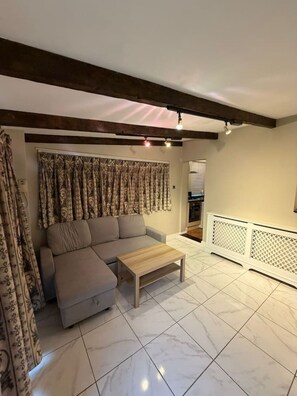 Un salon avec un canapé d’angle, une table basse, des rideaux à motifs et un radiateur blanc.