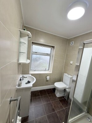 Une salle de bain avec des toilettes, un lavabo, une fenêtre et une douche.