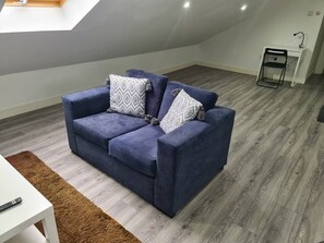 A modern living room with a blue sofa, patterned cushions, a brown rug, and a white desk. - SAV Stays 2 Bed Flat, Saffron Leicester-1st Floor (Leicester)