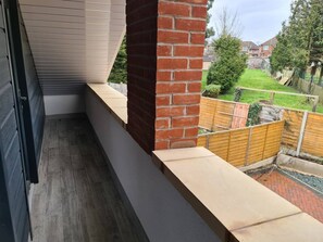 A balcony with a brick wall, a wooden fence, and a view of a residential area. - SAV Stays 2 Bed Flat, Saffron Leicester-1st Floor (Leicester)